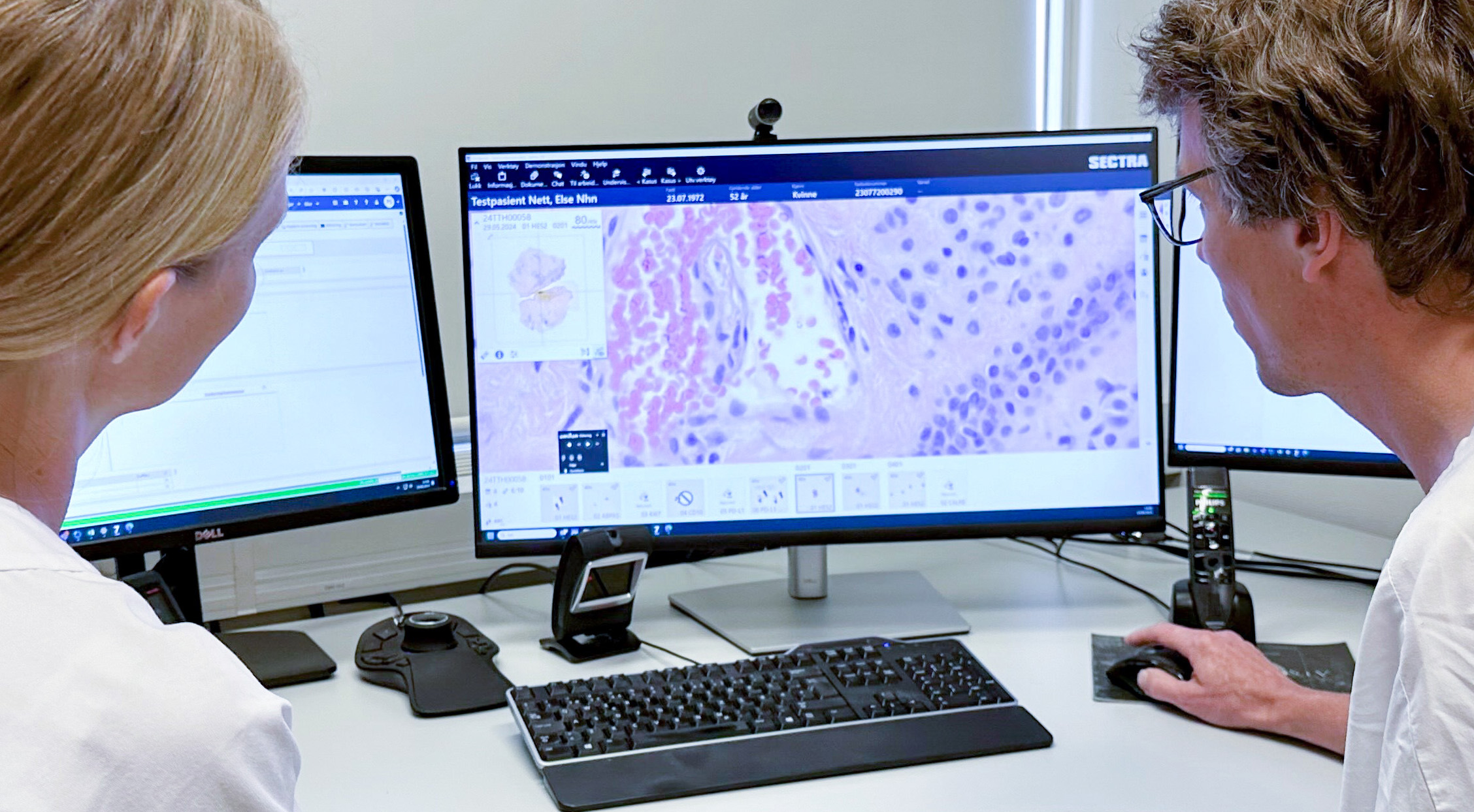 Mann og kvinne i legetøy ser på en dataskjerm som viser nærbilde av digitale vevsprøver. Foto.