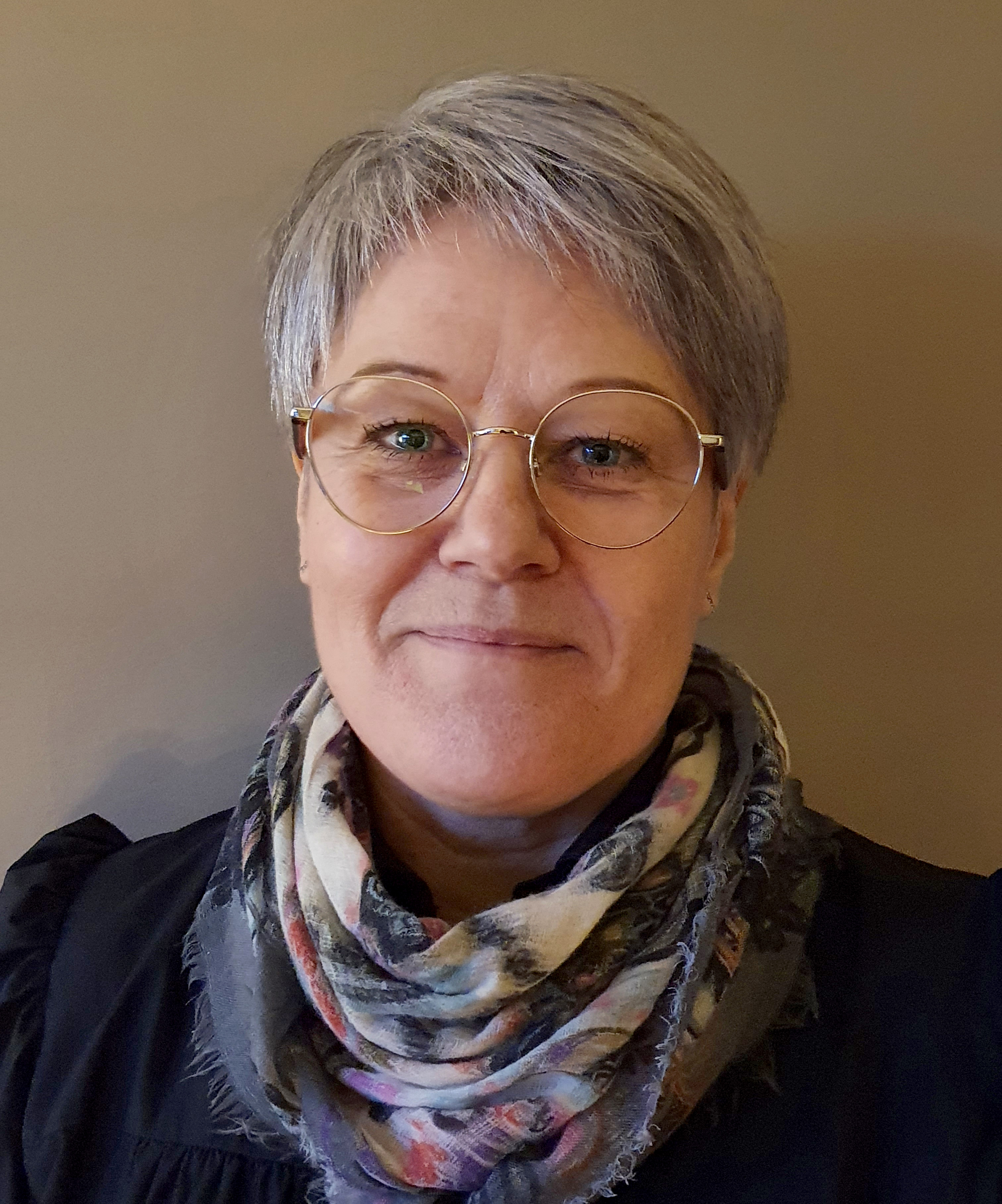 Smilende kvinne med kort, grått hår og briller.