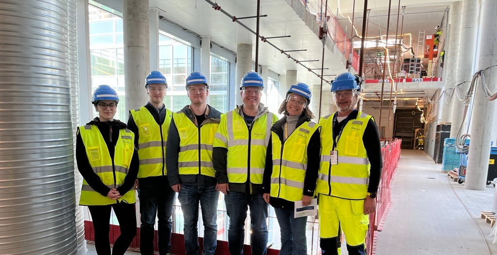 En gruppe menn og kvinner i sikkerhetsvester inne i et bygg på en byggeplass. Foto.