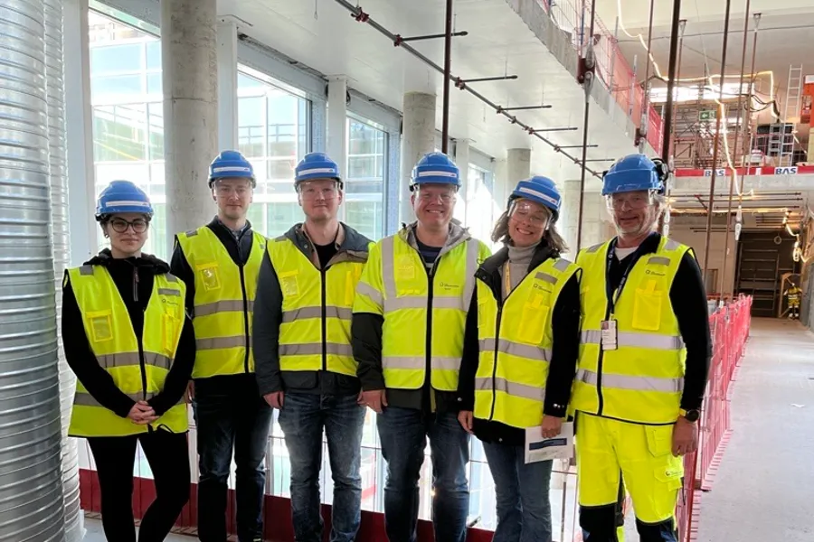 En gruppe menn og kvinner i sikkerhetsvester inne i et bygg på en byggeplass. Foto.