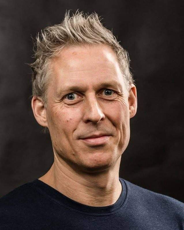 Smilende mann med kort, grått hår. Foto.