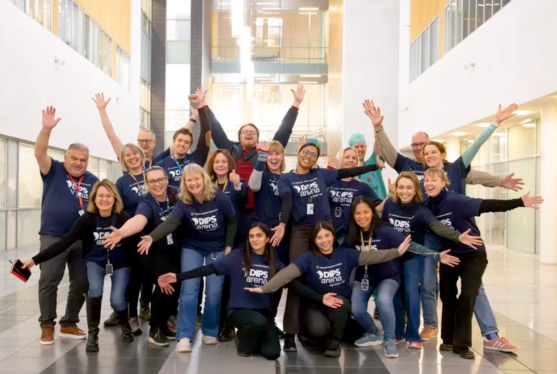 En stor gruppe mennesker med T-skjorter med "DIPS arena" på, som jubler og poserer for et bilde. Foto.
