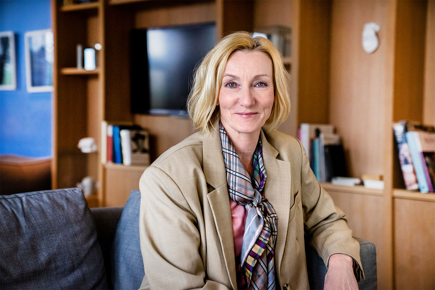 Smilende kvinne med blondt, halvlangt hår og beige dressjakke.